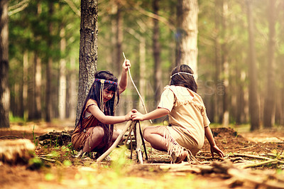 Buy stock photo Native American children, girl and outdoor for campfire with helping hand, teaching or learning. Kids, siblings and wood for flame with development of survival skill in forest with branches on ground