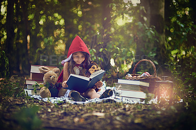 Buy stock photo Shot of a little girl in a red cape reading a book with her toys in the woods