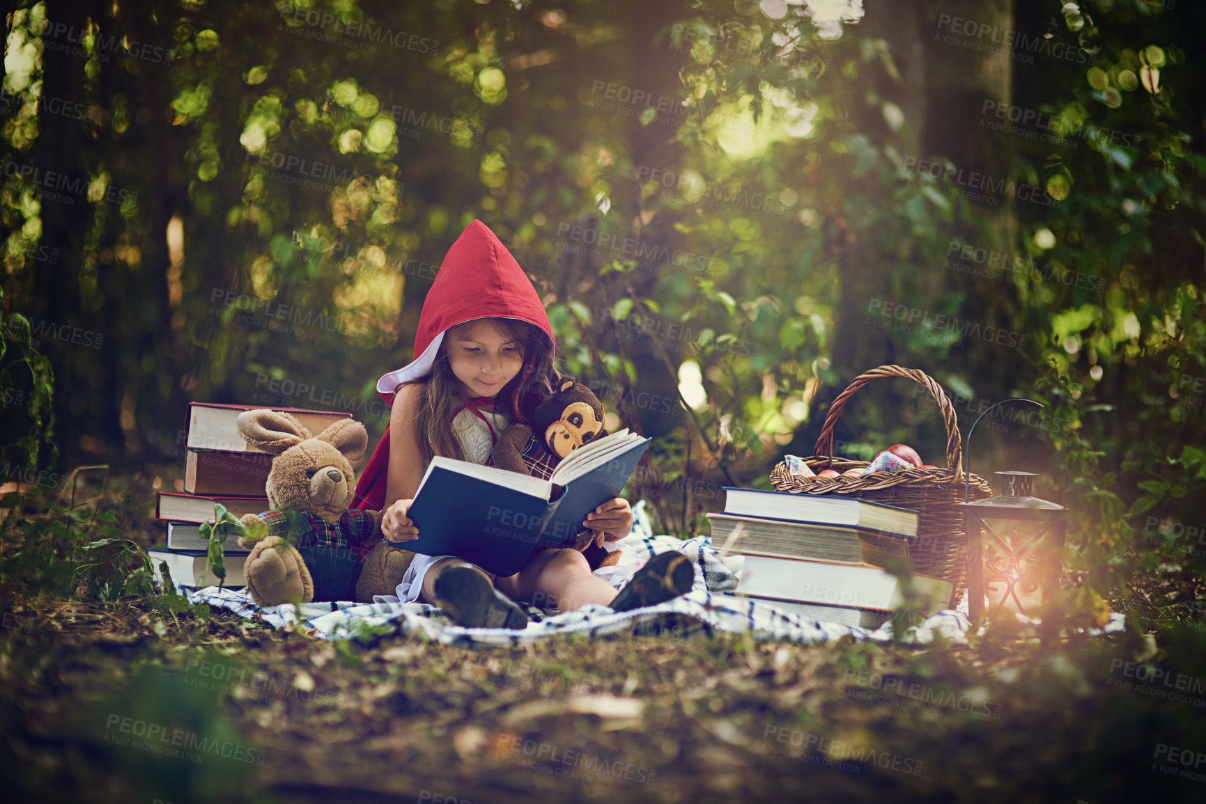 Buy stock photo Shot of a little girl in a red cape reading a book with her toys in the woods