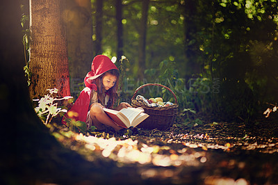 Buy stock photo Shot of a little girl in a red cape reading a book in the woods