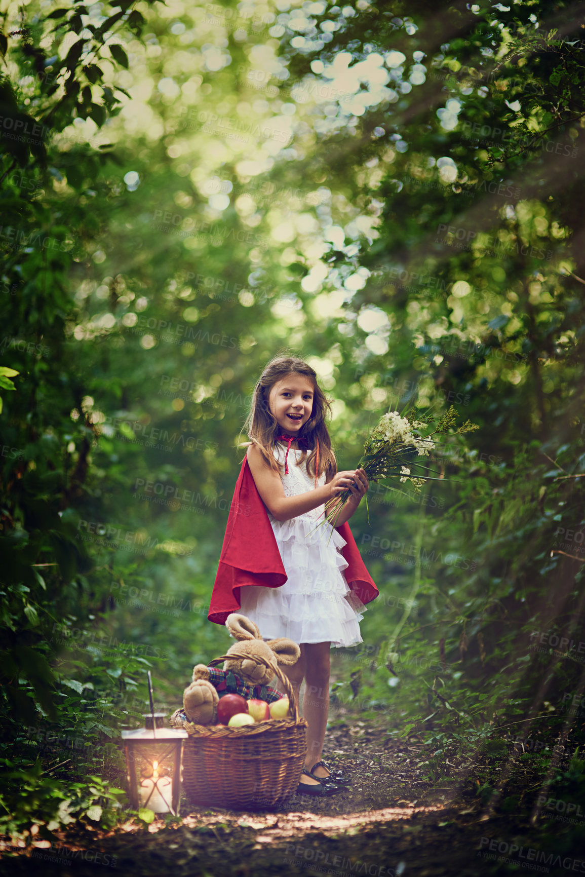 Buy stock photo Portrait of a little girl dressed in a red cape holding some flowers in the woods