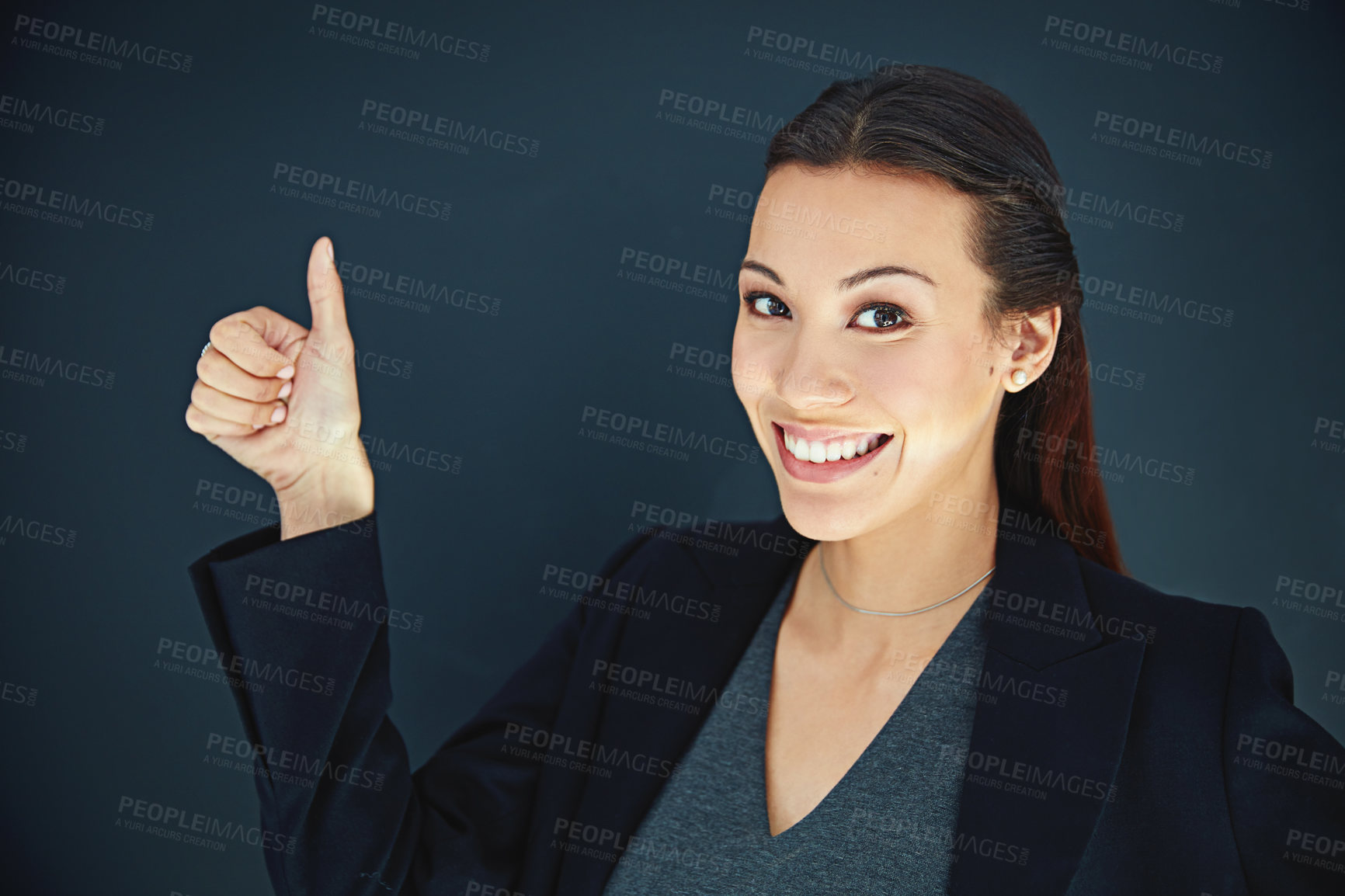 Buy stock photo Portrait of a young businesswoman showing a thumbs up against a dark background