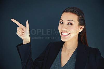 Buy stock photo Portrait of a young businesswoman pointing to the side against a dark background