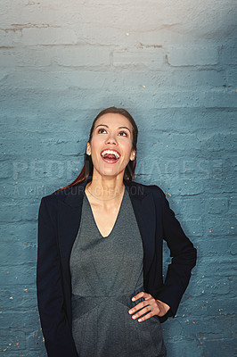 Buy stock photo Shot of a happy young businesswoman looking up while posing against a brick wall