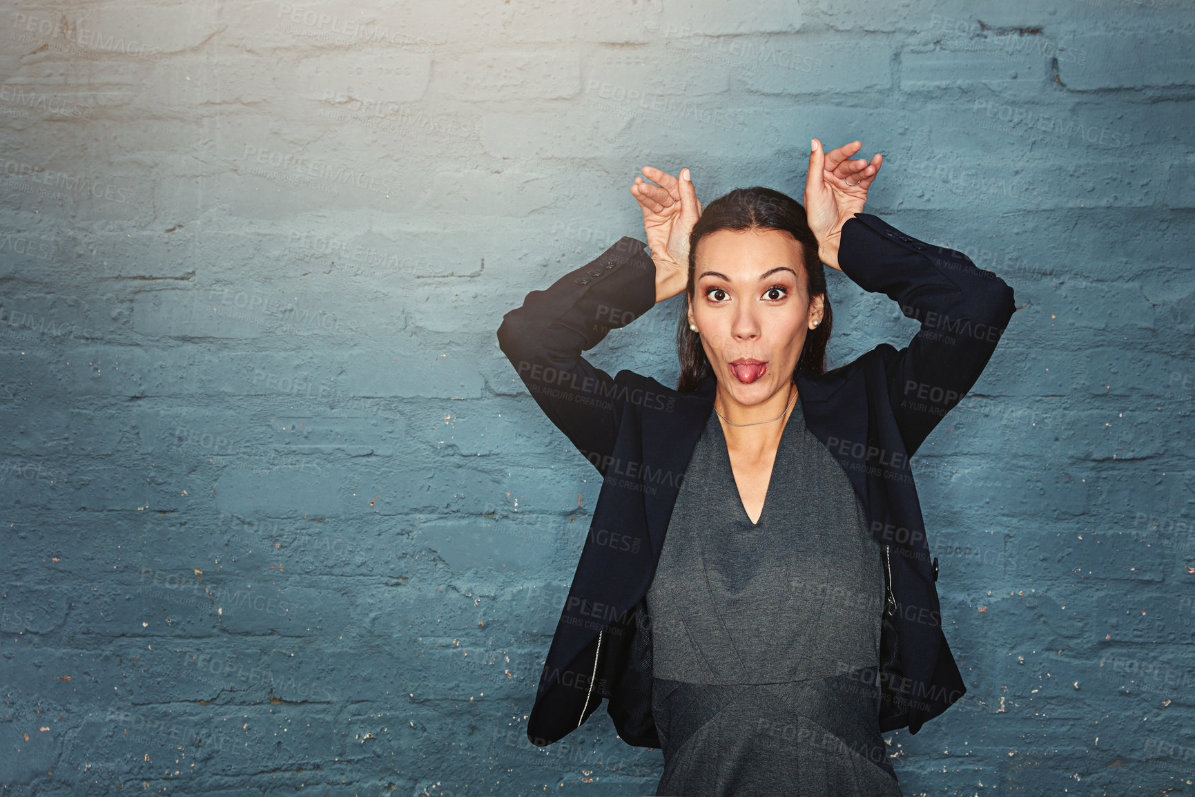 Buy stock photo Portrait of a silly businesswoman pulling a funny face while posing against a brick wall