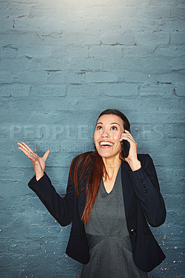 Buy stock photo Shot of an excited businesswoman answering her phone while standing against a brick wall