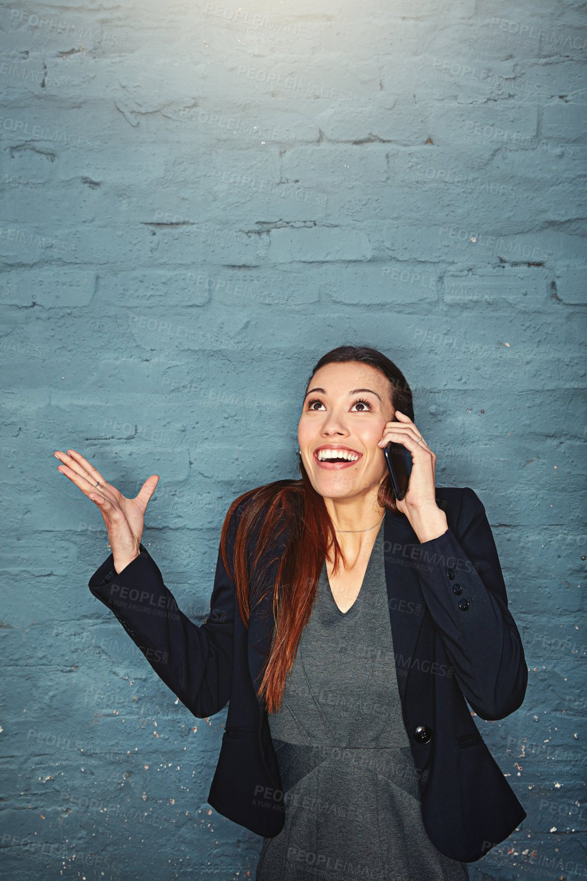 Buy stock photo Shot of an excited businesswoman answering her phone while standing against a brick wall