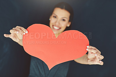 Buy stock photo Portrait of a young woman posing with a heart against a gray background