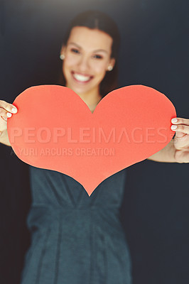 Buy stock photo Portrait of a young woman posing with a heart against a gray background