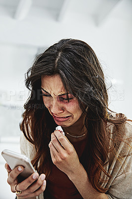 Buy stock photo Shot of a beaten and bruised young woman crying while looking at her cellphone