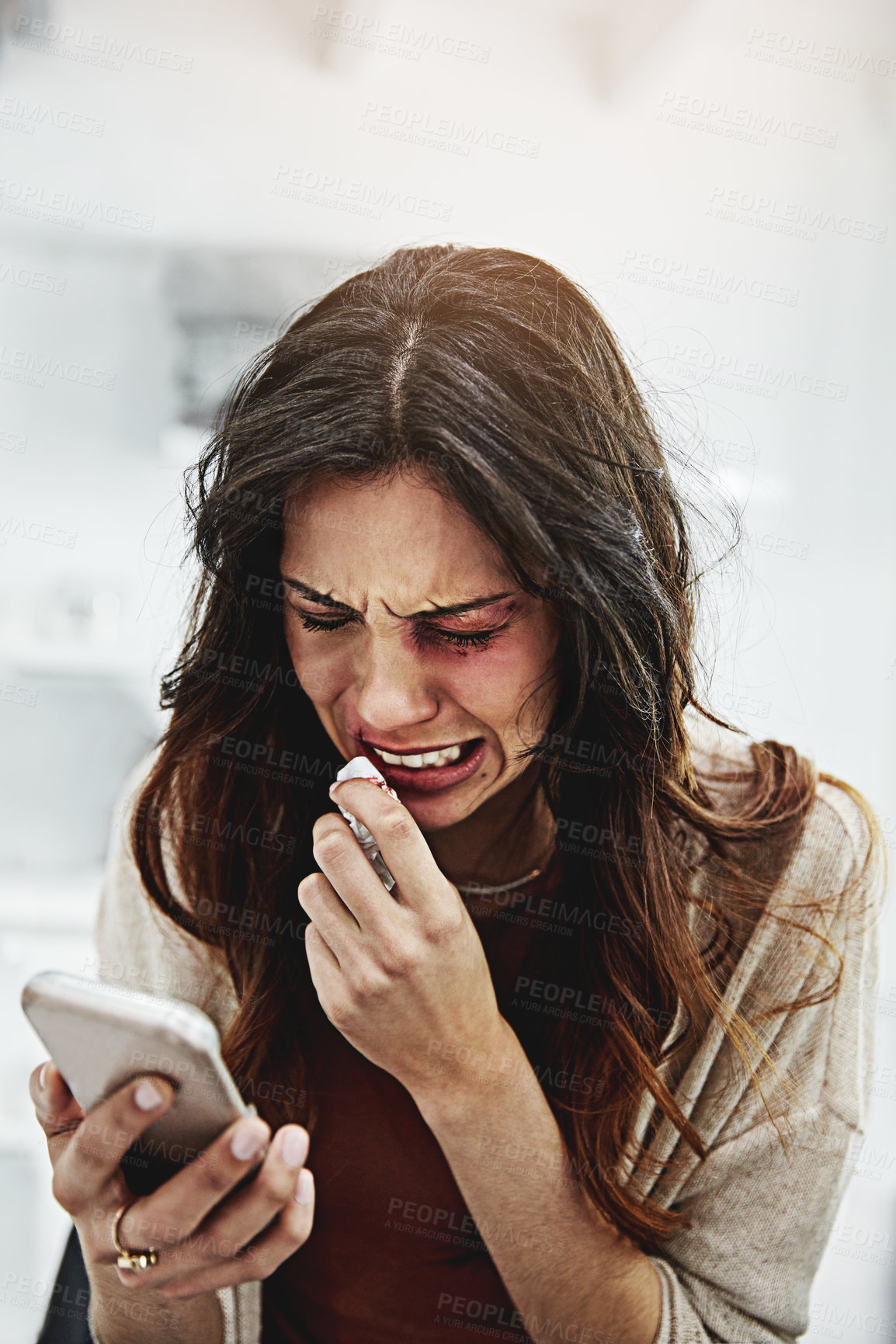 Buy stock photo Shot of a beaten and bruised young woman crying while looking at her cellphone