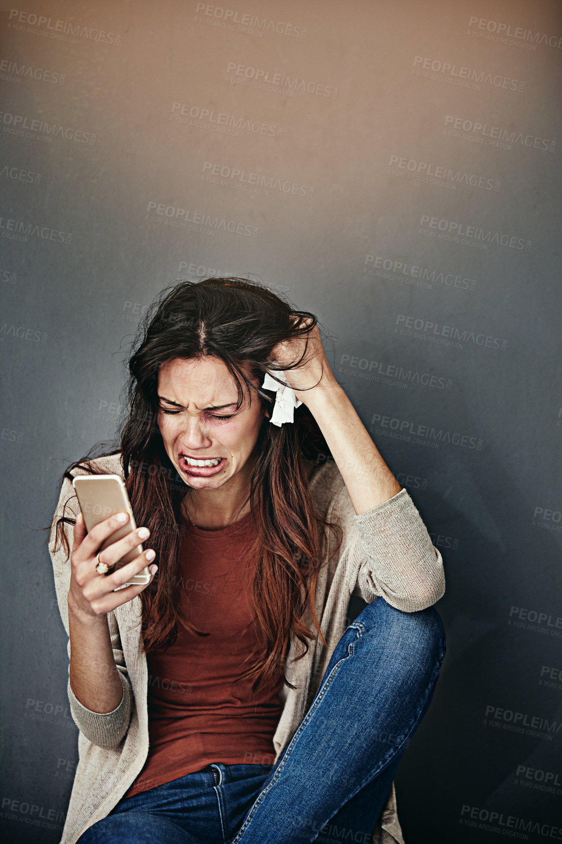 Buy stock photo Shot of a beaten and bruised young woman crying while looking at her cellphone