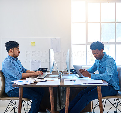 Buy stock photo Shot of a young man using a digital tablet at his desk in a modern office