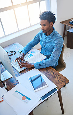 Buy stock photo Shot of a young man using a computer at his work desk in a modern office
