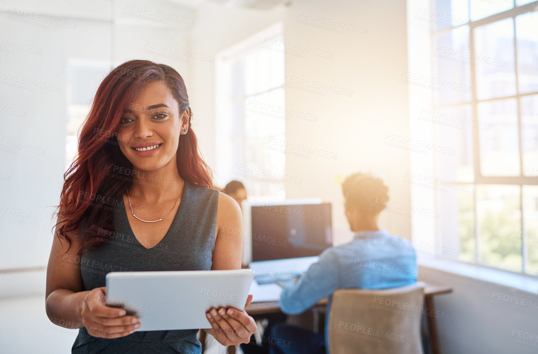 Buy stock photo Portrait of a young entrepreneur using a digital tablet at work with her team in the background