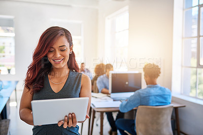 Buy stock photo Shot of a young entrepreneur using a digital tablet at work with her team in the background