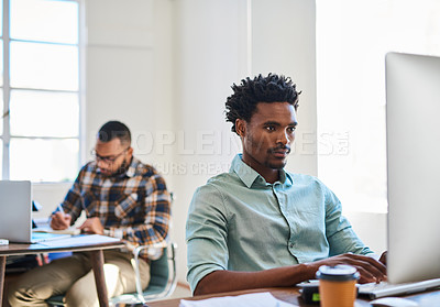 Buy stock photo Shot of a young man using a computer at his work desk in a modern office