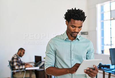 Buy stock photo Shot of a young entrepreneur using a digital tablet at work with his team in the background