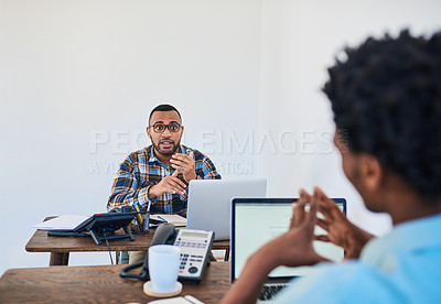 Buy stock photo Shot of two young coworkers having a discussion opposite each other in a modern office