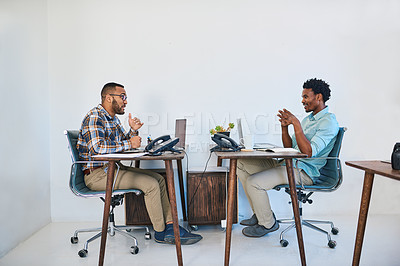 Buy stock photo Shot of two young coworkers having a discussion opposite each other in a modern office