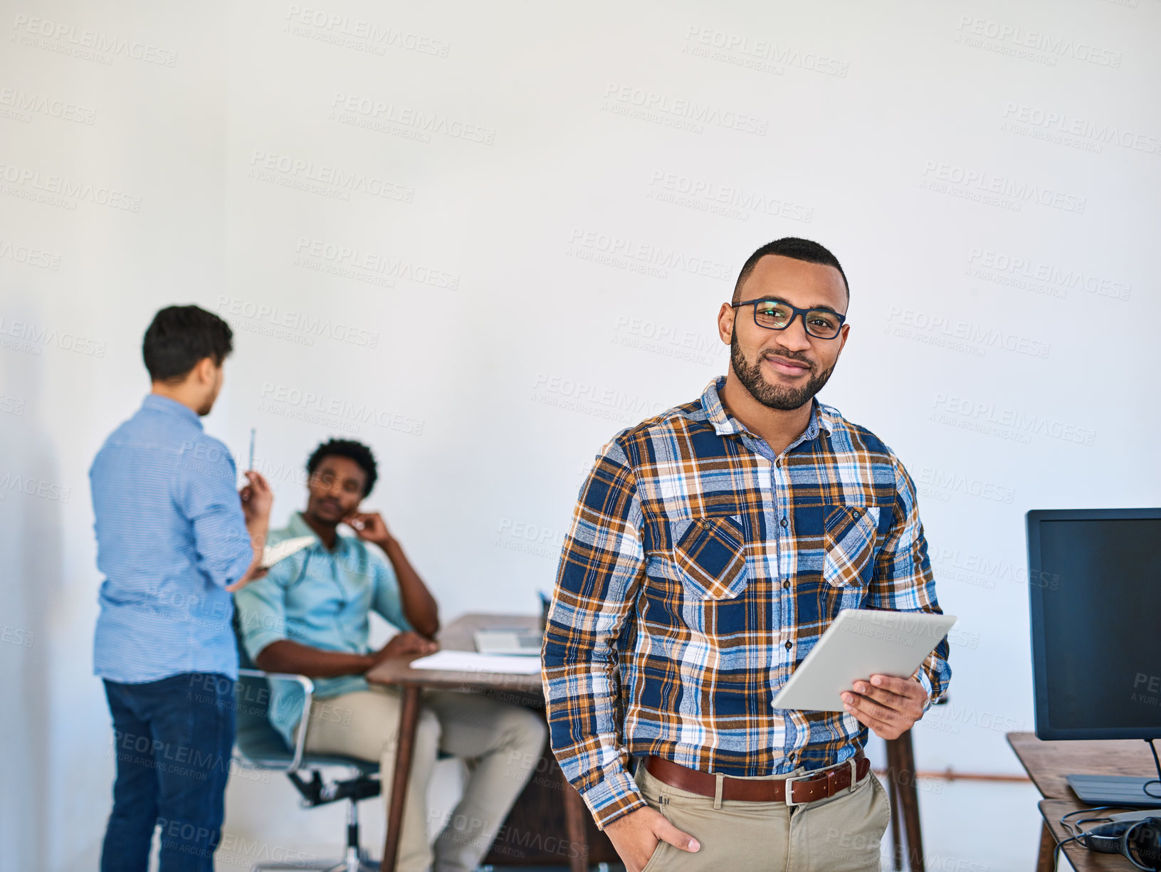 Buy stock photo Portrait of a young entrepreneur using a digital tablet at work with his team in the background