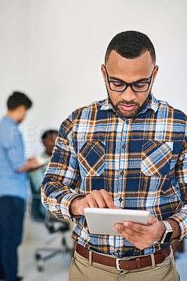 Buy stock photo Shot of a young entrepreneur using a digital tablet at work with his team in the background