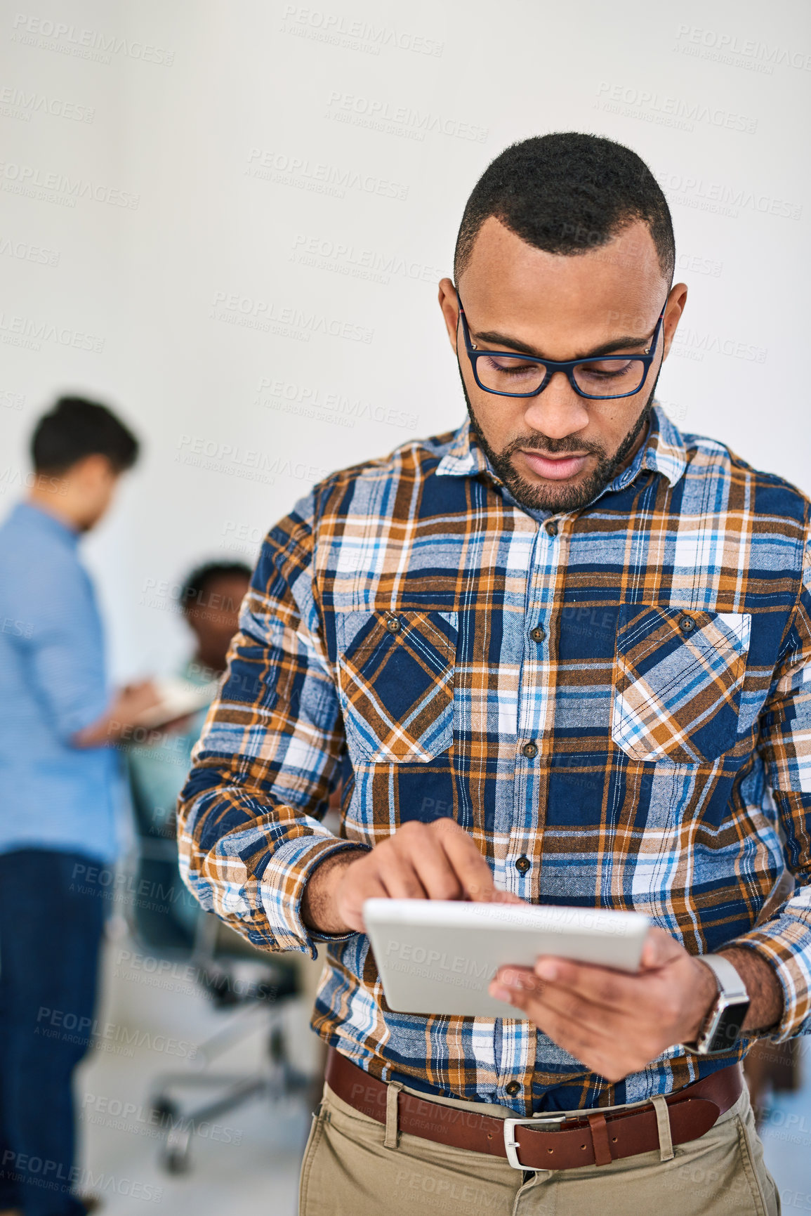 Buy stock photo Shot of a young entrepreneur using a digital tablet at work with his team in the background