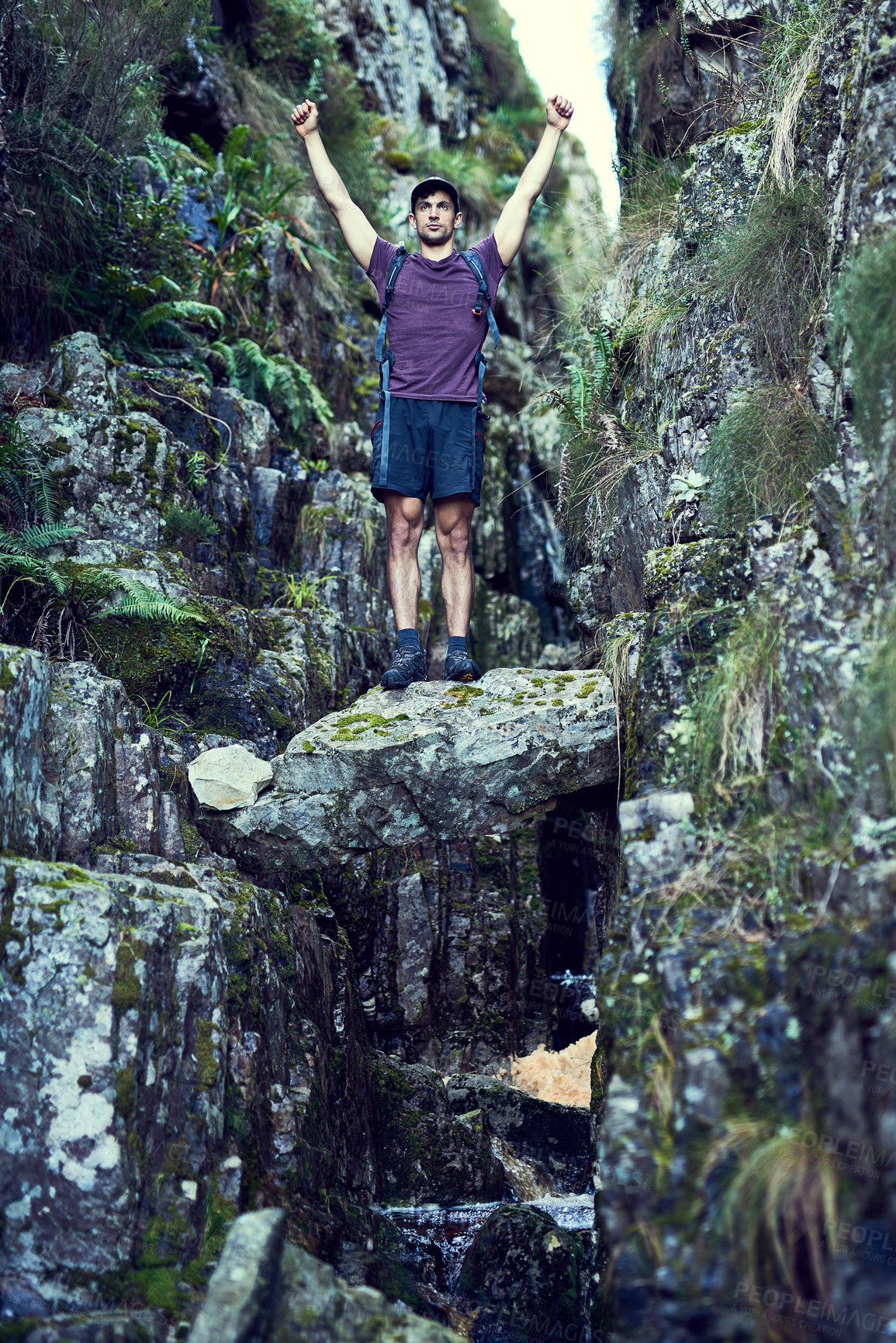Buy stock photo Shot of a young man raising his hands while exploring a hiking trail alone