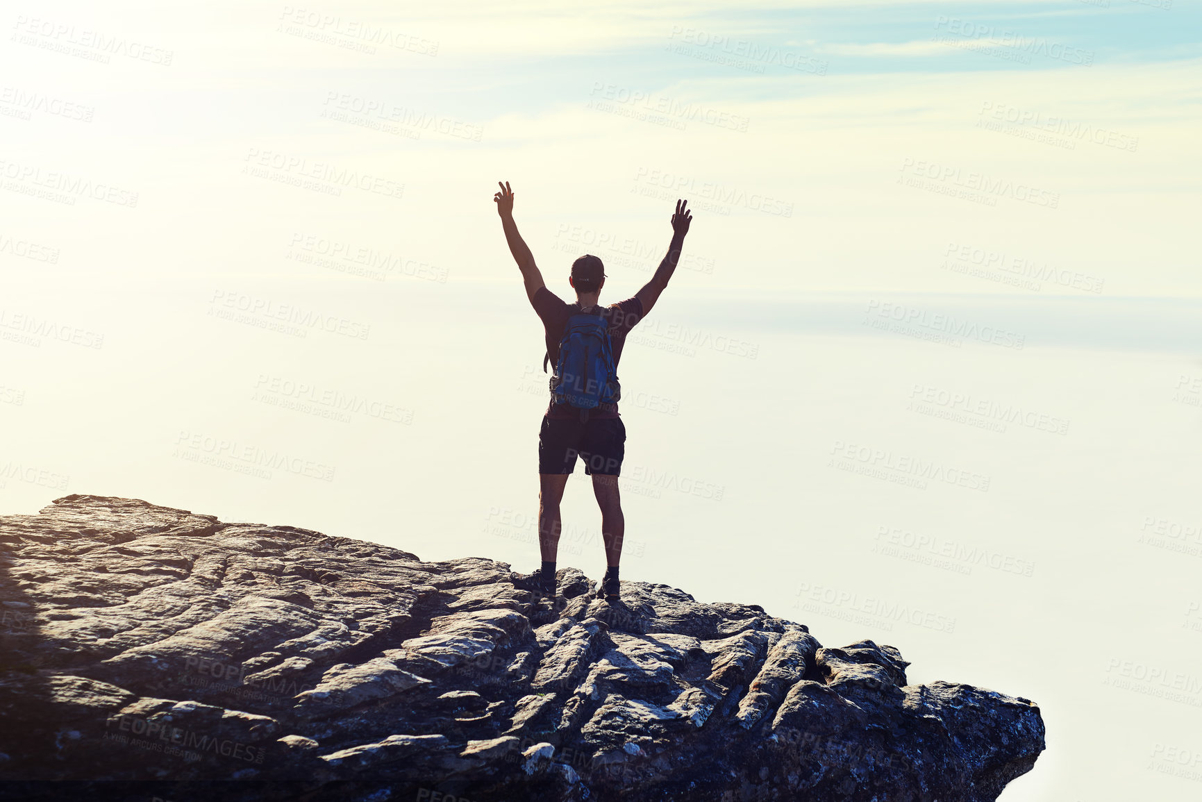 Buy stock photo Rearview shot of an unidentifiable young man raising his arms in triumph on a mountaintop