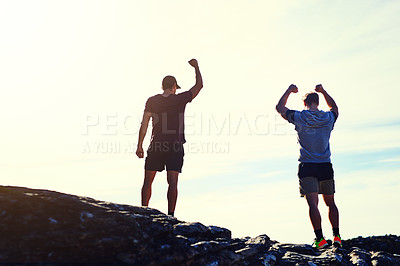 Buy stock photo Rearview shot of two unidentifiable young men raising their arms in triumph on a mountaintop