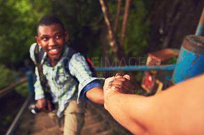 Buy stock photo Cropped shot of a young man helping a friend up a mountain trail