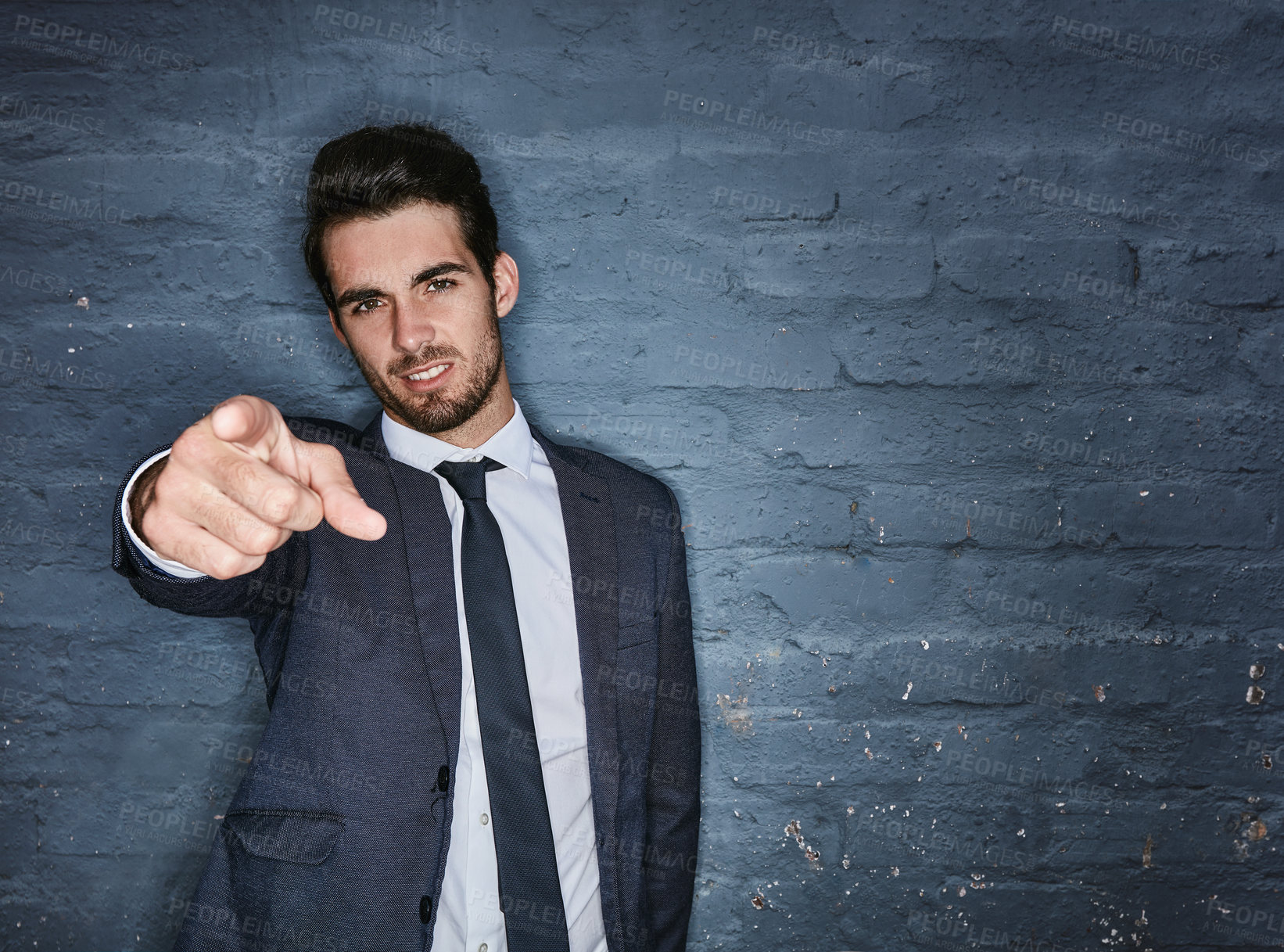 Buy stock photo Shot of a handsome businessman pointing towards you against a grey brick wall