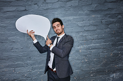 Buy stock photo Shot of a businessman holding a speech bubble against a grey wall