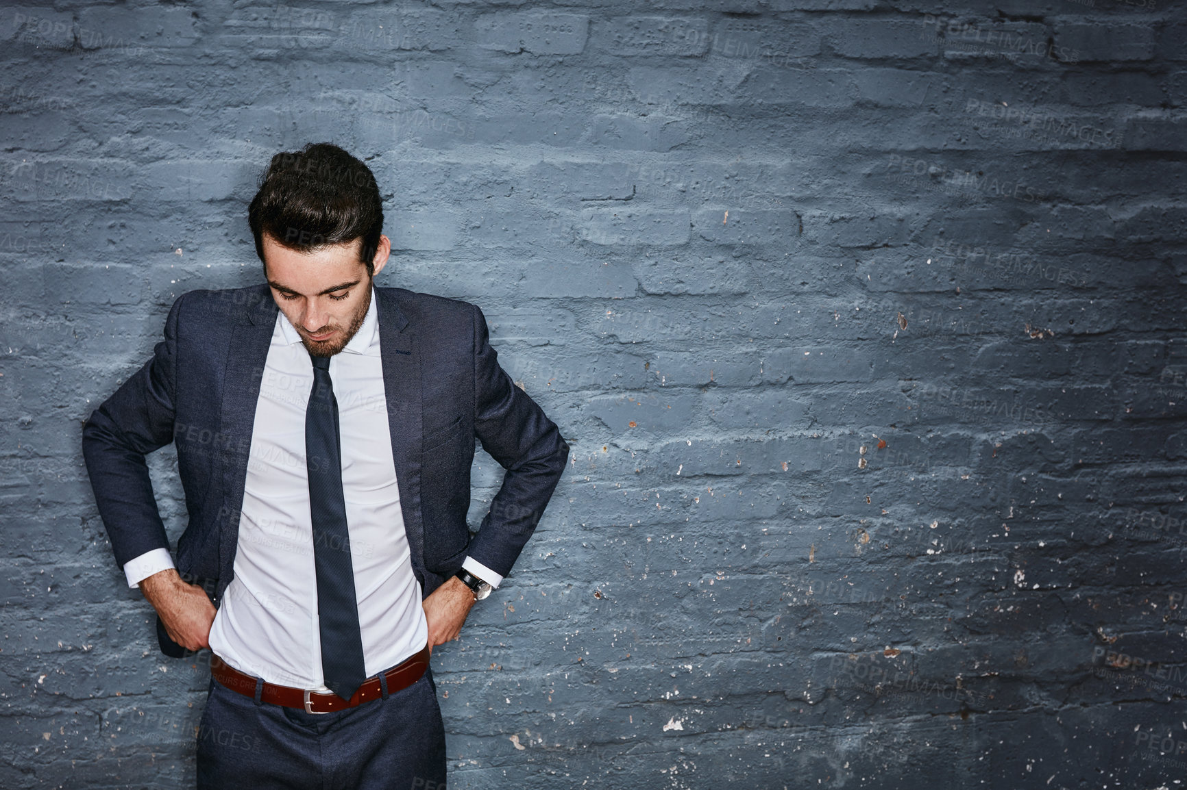 Buy stock photo Shot of a businessman adjusting his pants against a grey wall