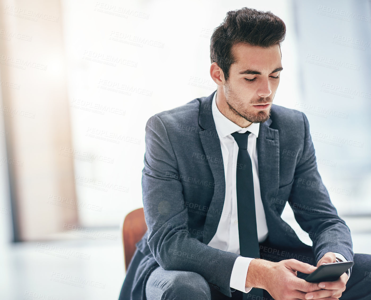 Buy stock photo Shot of a focussed young businessman using his smartphone in the office