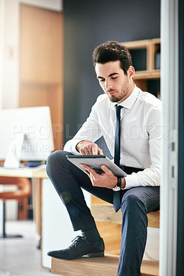 Buy stock photo Shot of a trendy young businessman using his tablet while sitting on the stairs in his office