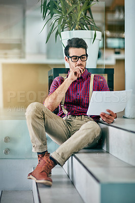 Buy stock photo Full length shot of a handsome young designer looking at paperwork in his office