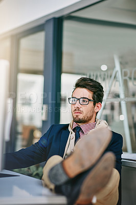 Buy stock photo Shot of a trendy young businessman sitting with his feet on the desk while using his computer