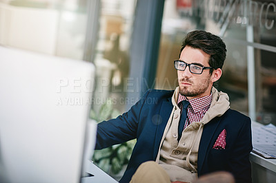 Buy stock photo Shot of a trendy young businessman sitting with his feet on the desk while using his computer