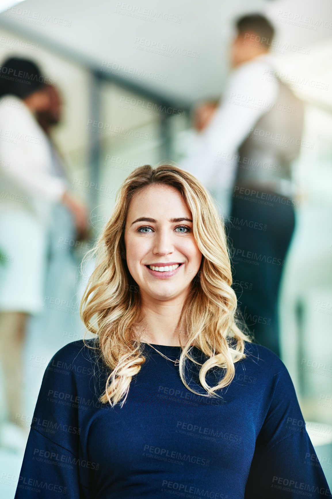 Buy stock photo Closeup portrait of a happy, joyful and confident corporate businesswoman standing in an office. Beautiful blonde female smiling and cheerful with her colleagues in the blurred background