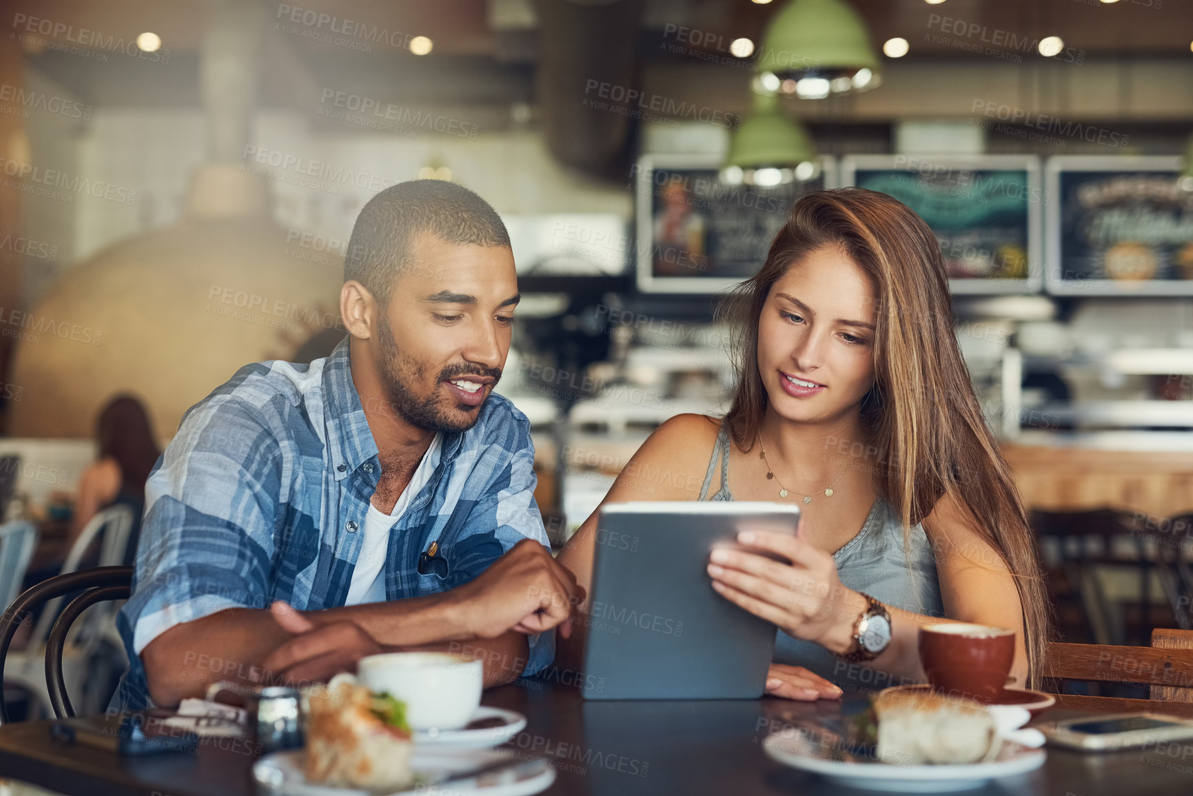 Buy stock photo Cropped shot of a young couple using a digital tablet while sitting in a cafe