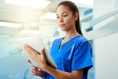 Buy stock photo Shot of a young nurse using a tablet while standing inside a clinic