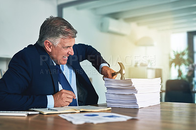 Buy stock photo Shot of a frustrated businessman hitting a pile of paperwork with a hammer