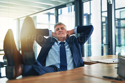 Buy stock photo Shot of a contented businessman relaxing with his feet on his desk