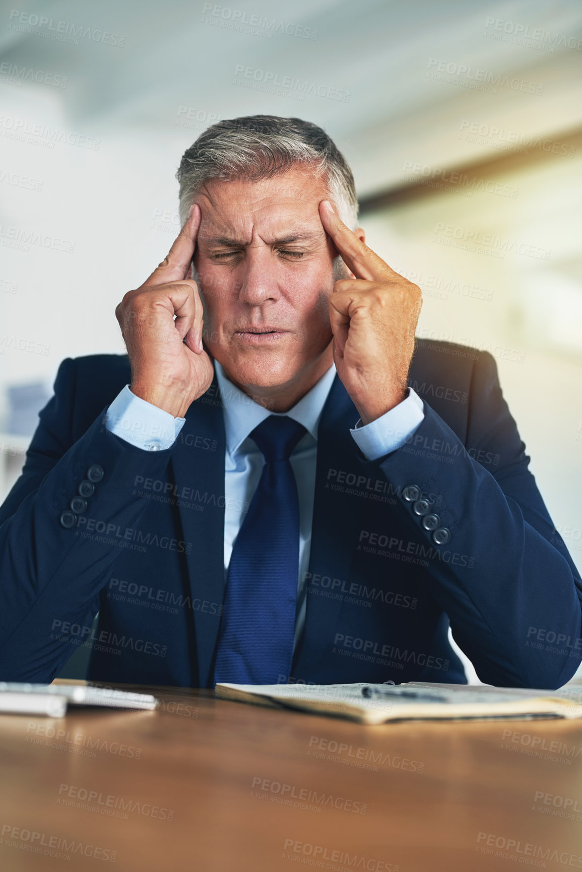 Buy stock photo Shot of a stressed businessman holding his fingers to his temples while sitting at his desk