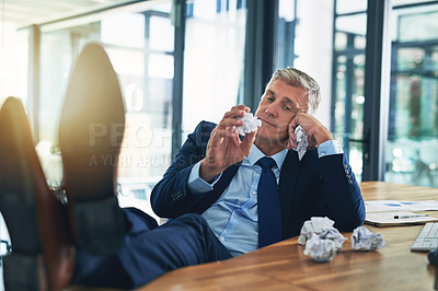 Buy stock photo Shot of a bored businessman crumpling pieces of paper at his desk