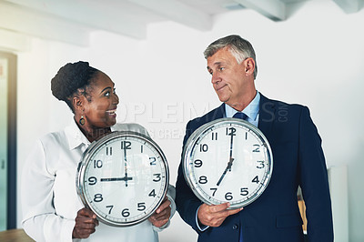 Buy stock photo Shot of two businesspeople holding clocks while posing in the office