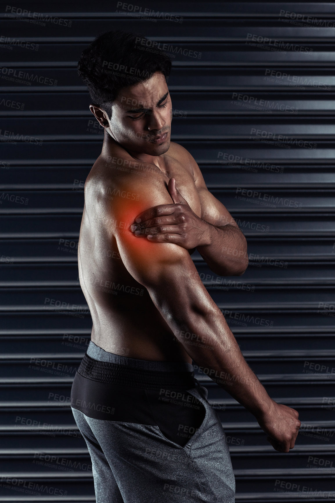 Buy stock photo Cropped shot of an athletic young man holding his shoulder in pain during a workout