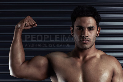 Buy stock photo Cropped portrait of an athletic young man flexing his bicep against a dark background