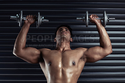 Buy stock photo Cropped shot of an athletic young man working out with dumbbells